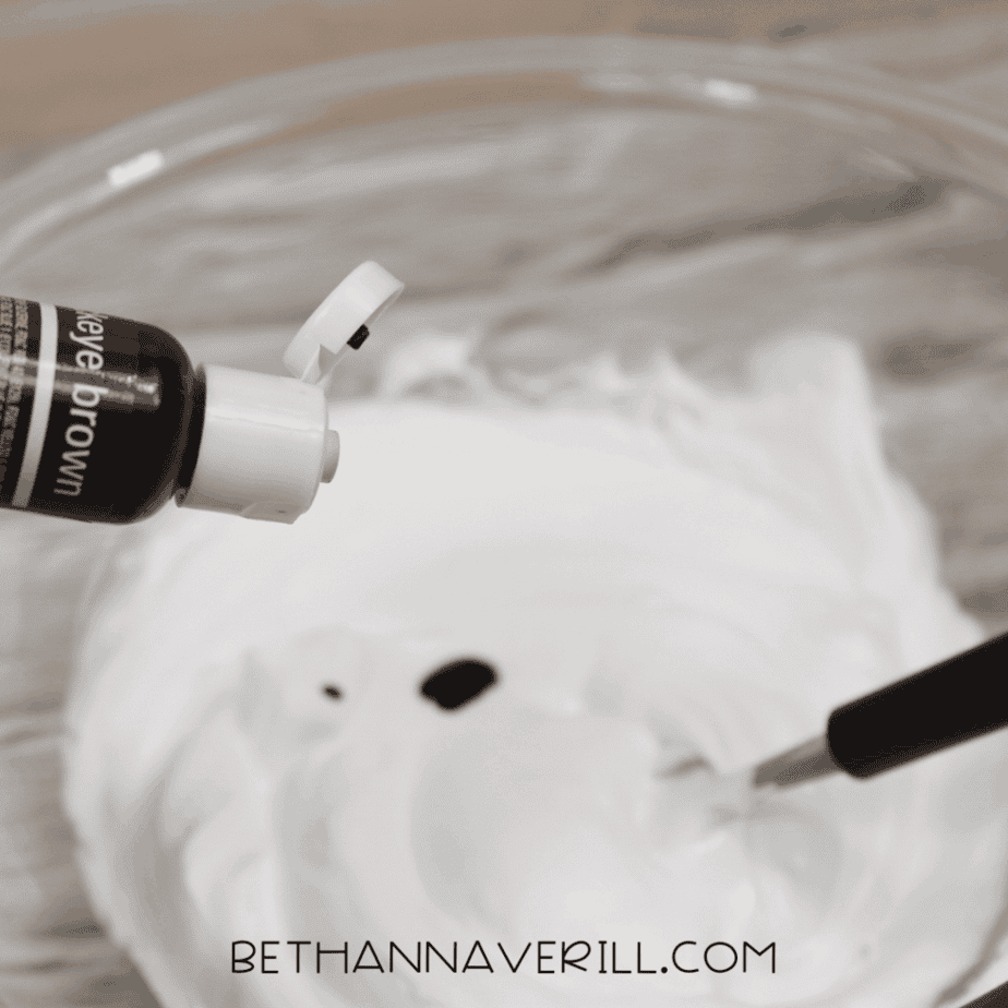 Brown food coloring being squeezed into a bowl of white shaving cream.