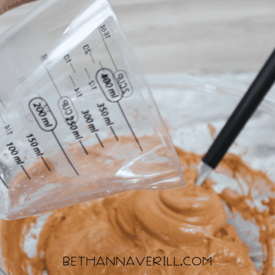 solution being poured from a measuring cup into a bowl of brown fluffy slime.