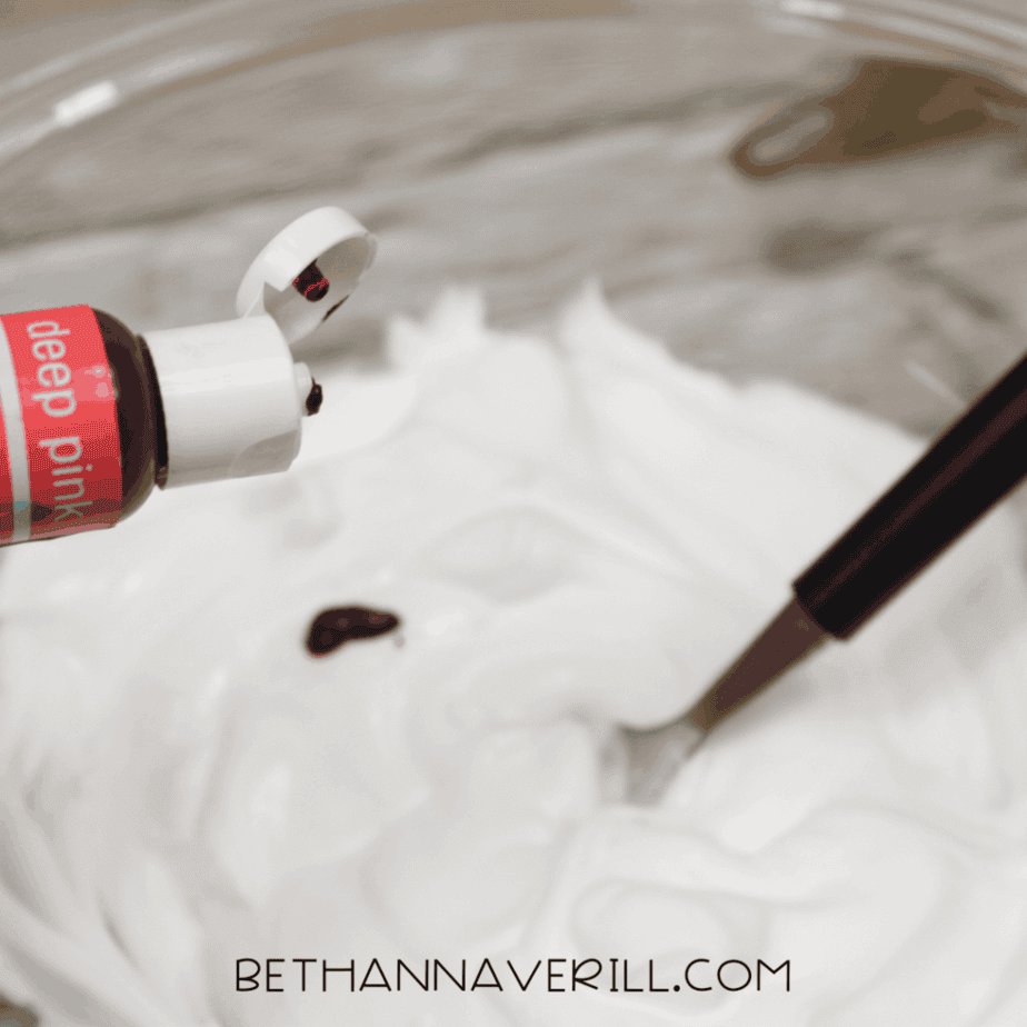 Pink food coloring being squeezed into a bowl of white shaving cream.