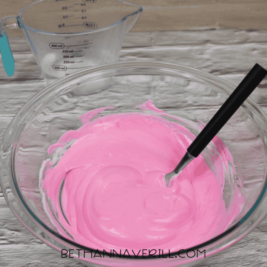 Pink fluffy slime being stirred in a glass bowl with a spoon.
