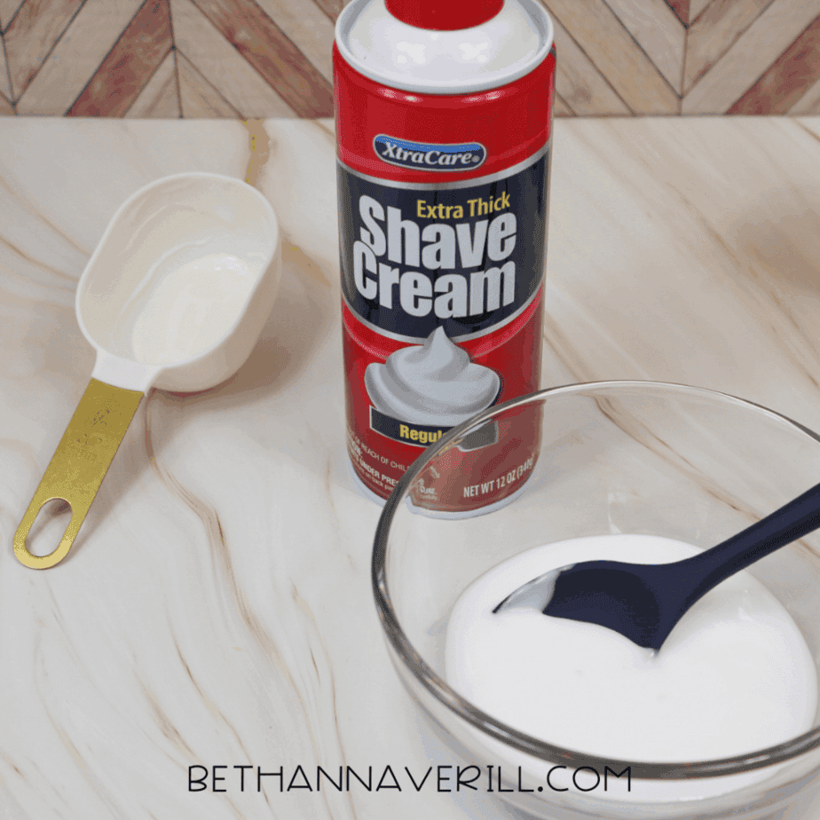Shaving cream dispensed into a clear glass bowl next to a measuring cup and spoon.