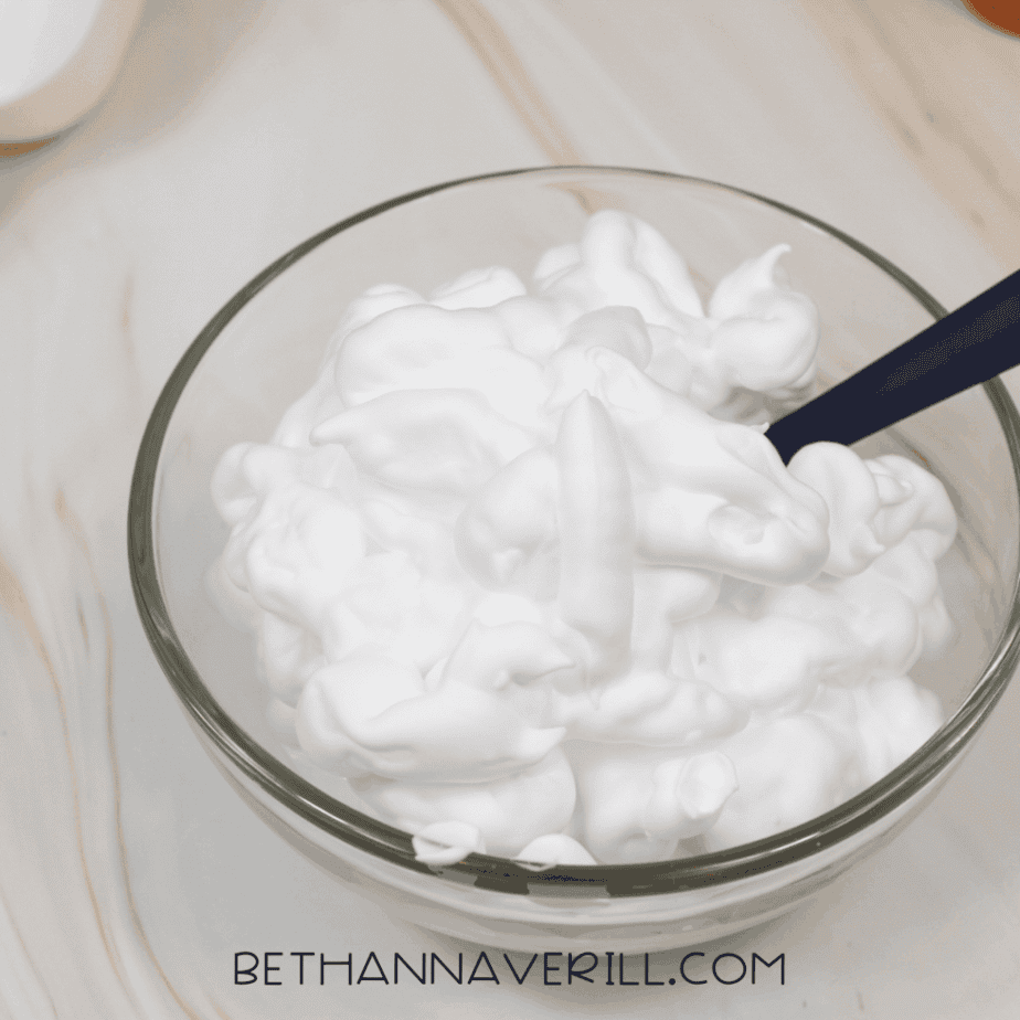 Glass bowl filled with white shaving cream with a spoon resting inside.