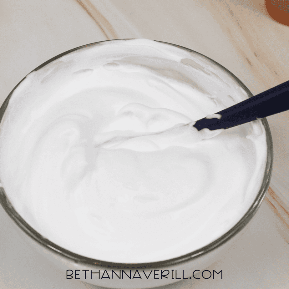 Spoon stirring white shaving cream inside a glass bowl.