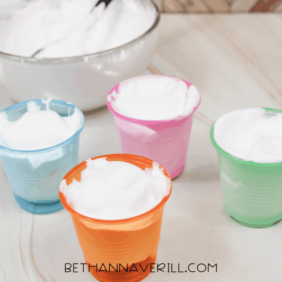 Shaving cream scooped into small plastic cups in blue, pink, orange, and green.