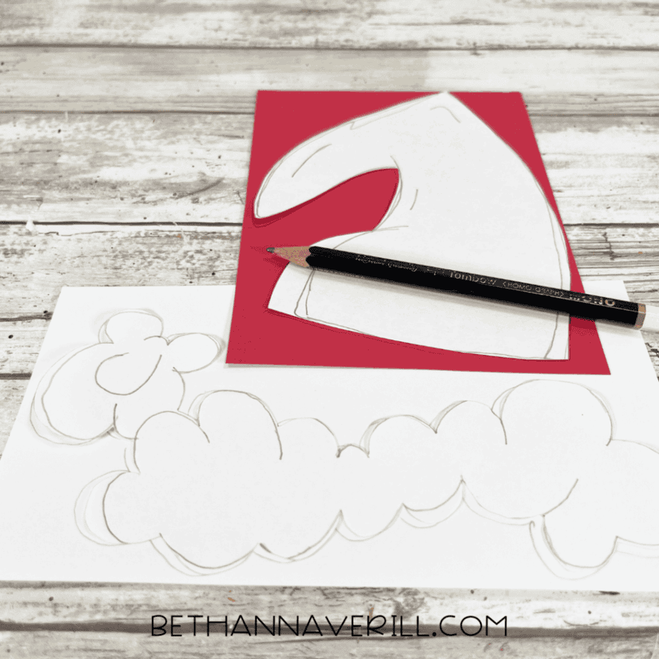 Red and white cardstock with pencil-drawn shapes for a Santa hat and fluffy trim pieces, with a pencil placed across the red cardstock.