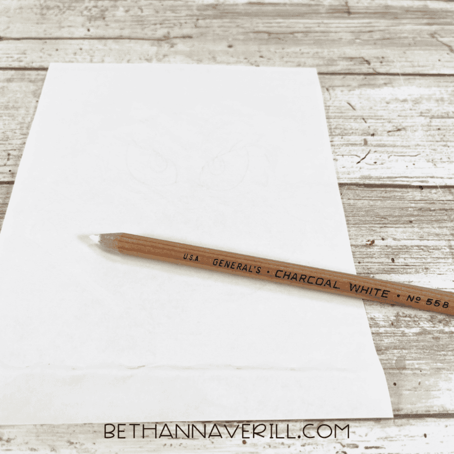 White paper with faint pencil sketches visible and a white charcoal pencil placed diagonally across the page.