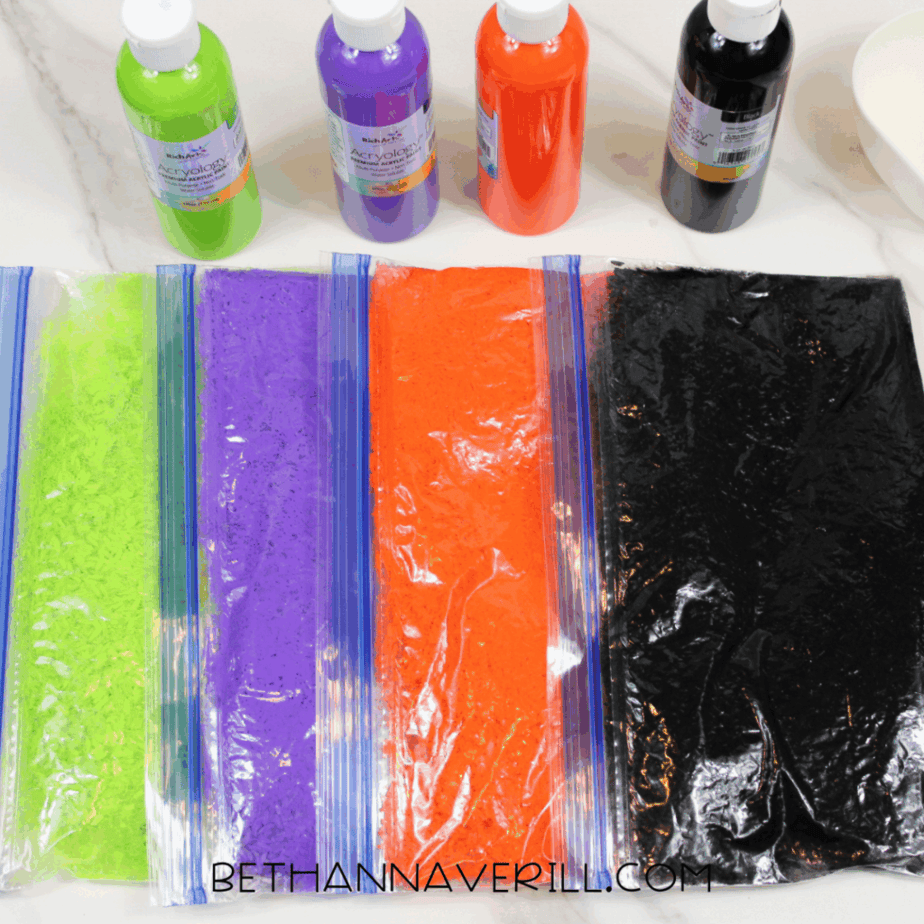 Resealable bags of rice dyed green, purple, orange, and black laid flat in a row to show evenly colored Halloween rice.