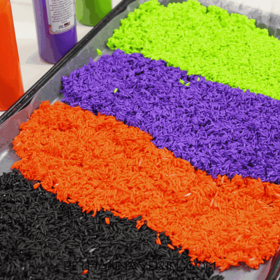 Close-up of green, purple, orange, and black colored rice spread out on a baking sheet to dry.