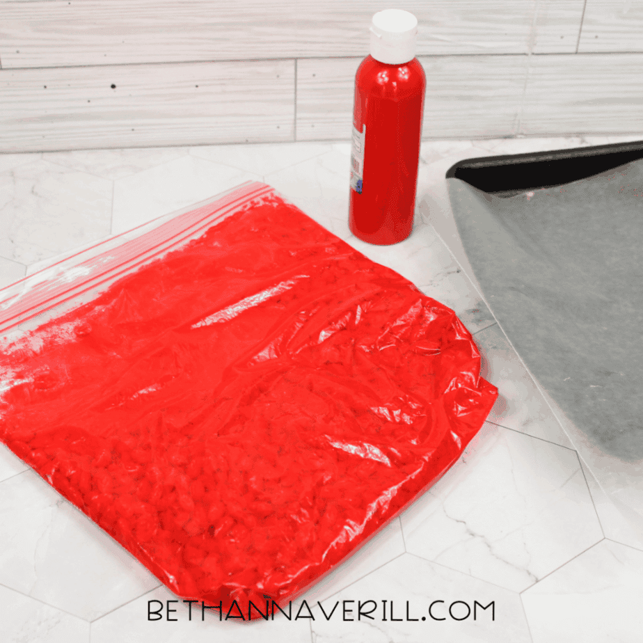 Zip-top bag of white beans fully coated in red paint for a ladybug sensory bin, resting on a countertop.