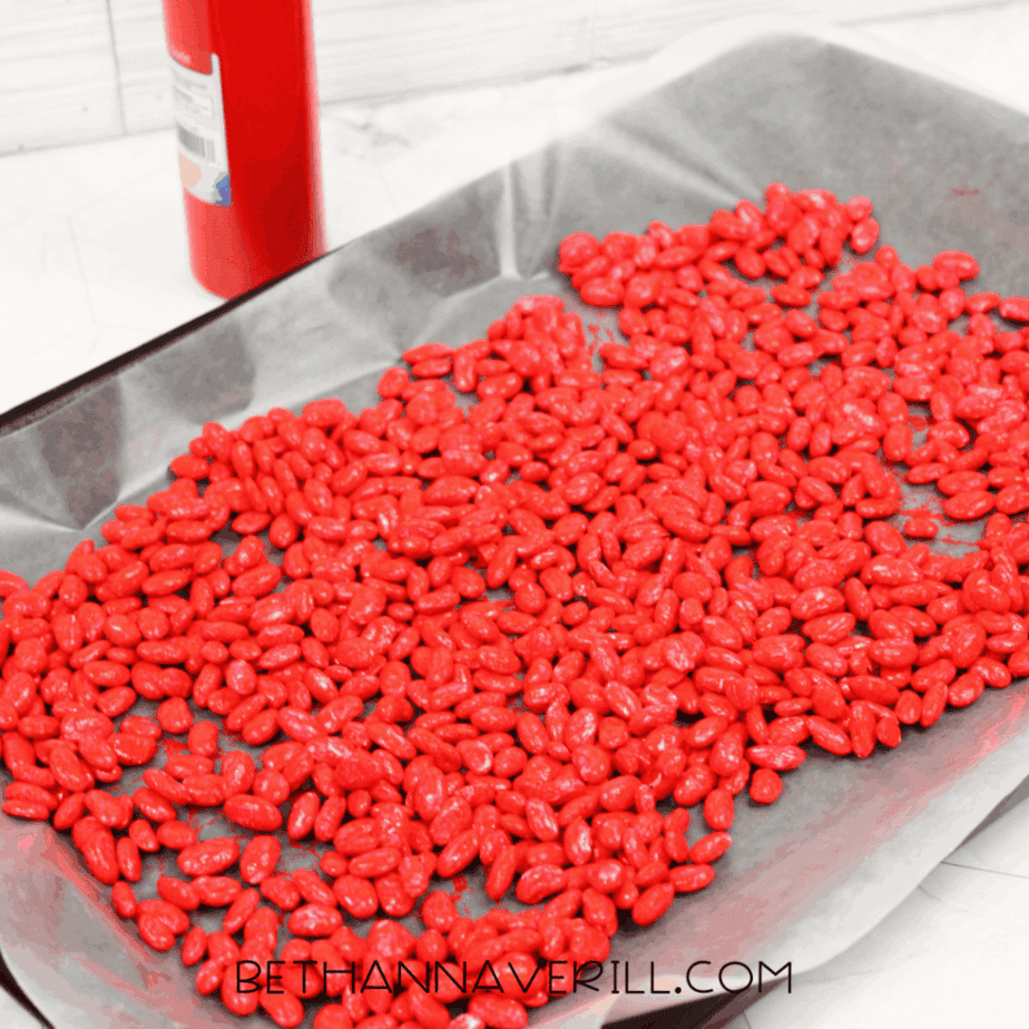 Painted red beans spread out on a wax-paper-lined baking sheet to dry for a ladybug sensory bin.