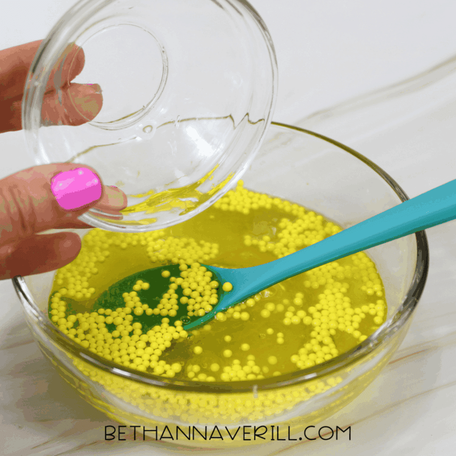 Activator solution being poured into yellow slime mixture with foam beads.
