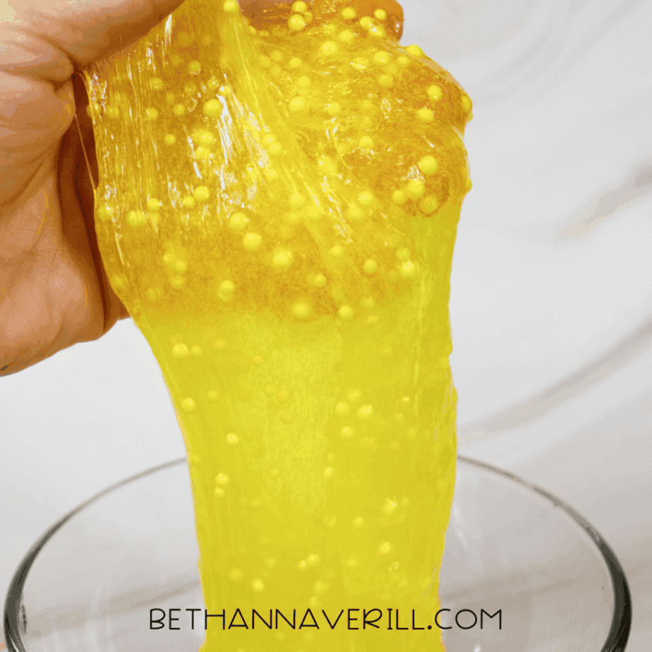Hand lifting and stretching yellow lemonade slime to show texture and bead distribution.