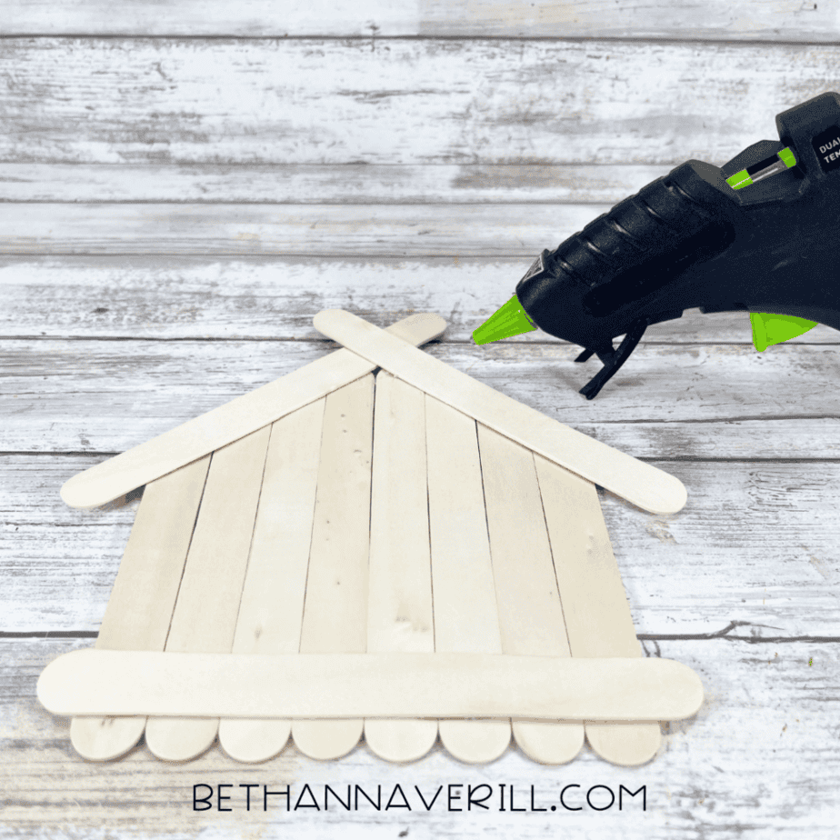 Popsicle stick structure with two angled craft sticks glued at the top, forming a roof shape on a white wood surface.