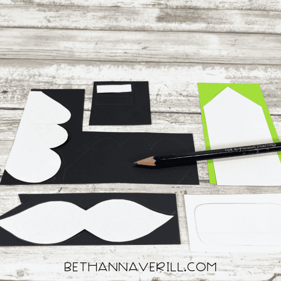 Black cardstock pieces cut into shapes and traced with pencil, arranged on a white wood background.