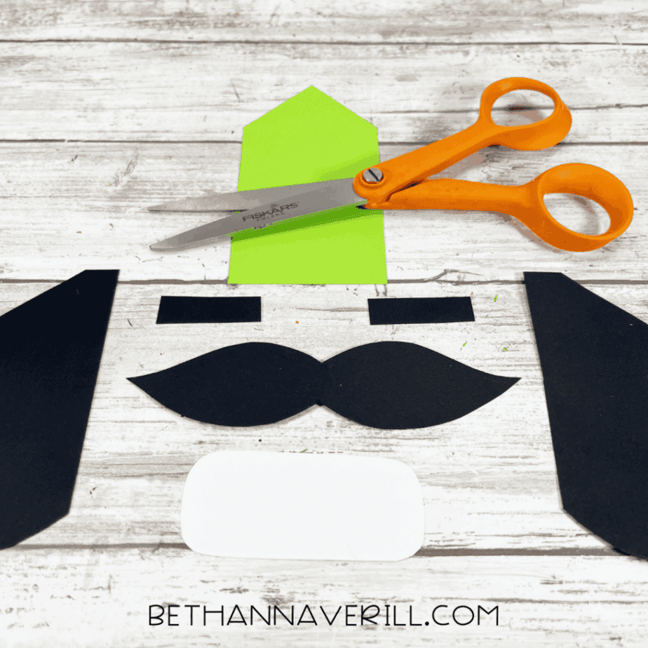 Black and white cardstock shapes cut out and laid flat on a white wood surface, with green cardstock and scissors nearby.