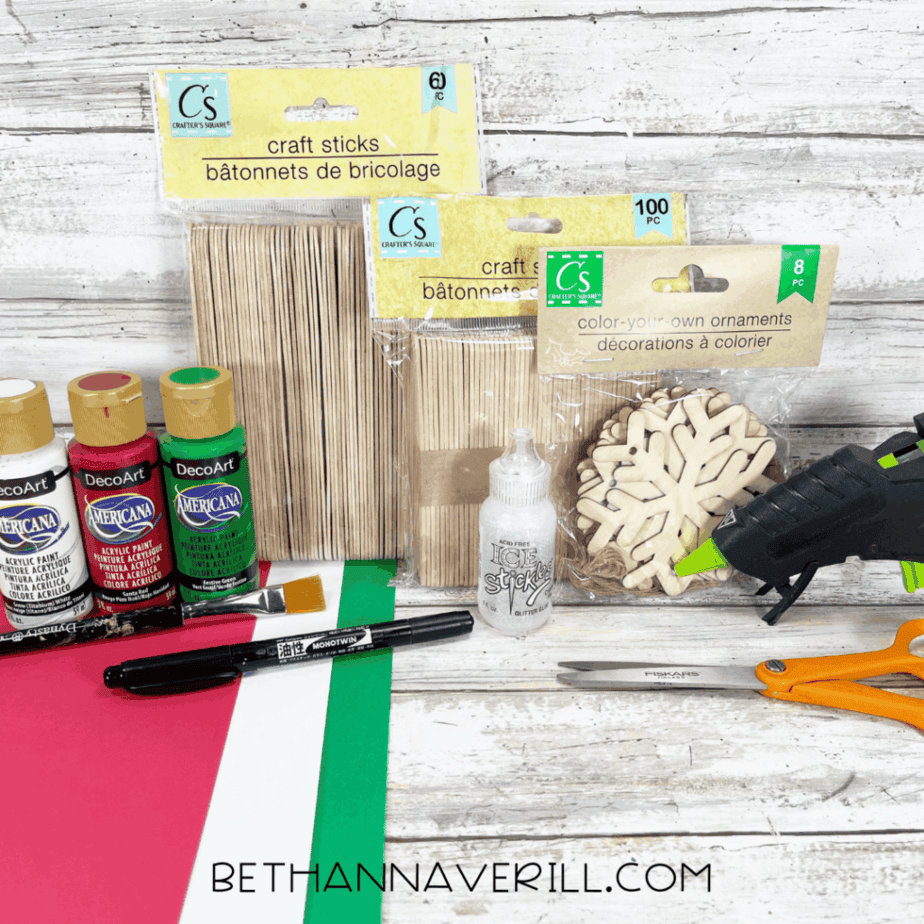 Supplies for Santa Magic Key popsicle stick craft including craft sticks, acrylic paint, wooden snowflakes, glue gun, scissors, and cardstock.