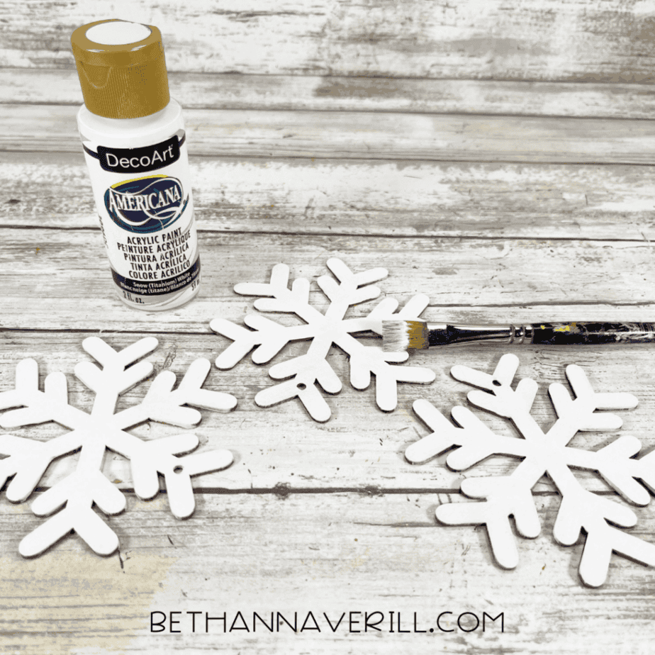 Wooden snowflake ornaments painted white for a Santa Magic Key craft with acrylic paint and a paintbrush.