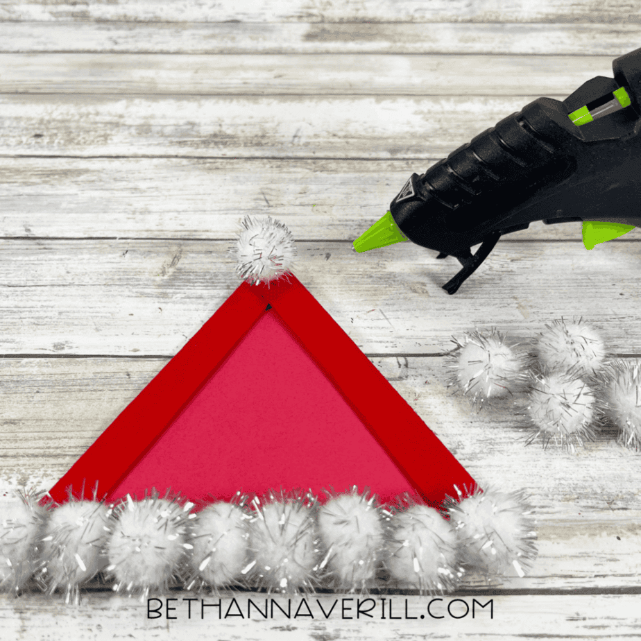 Single white pom pom attached at the top point of a red craft stick triangle.