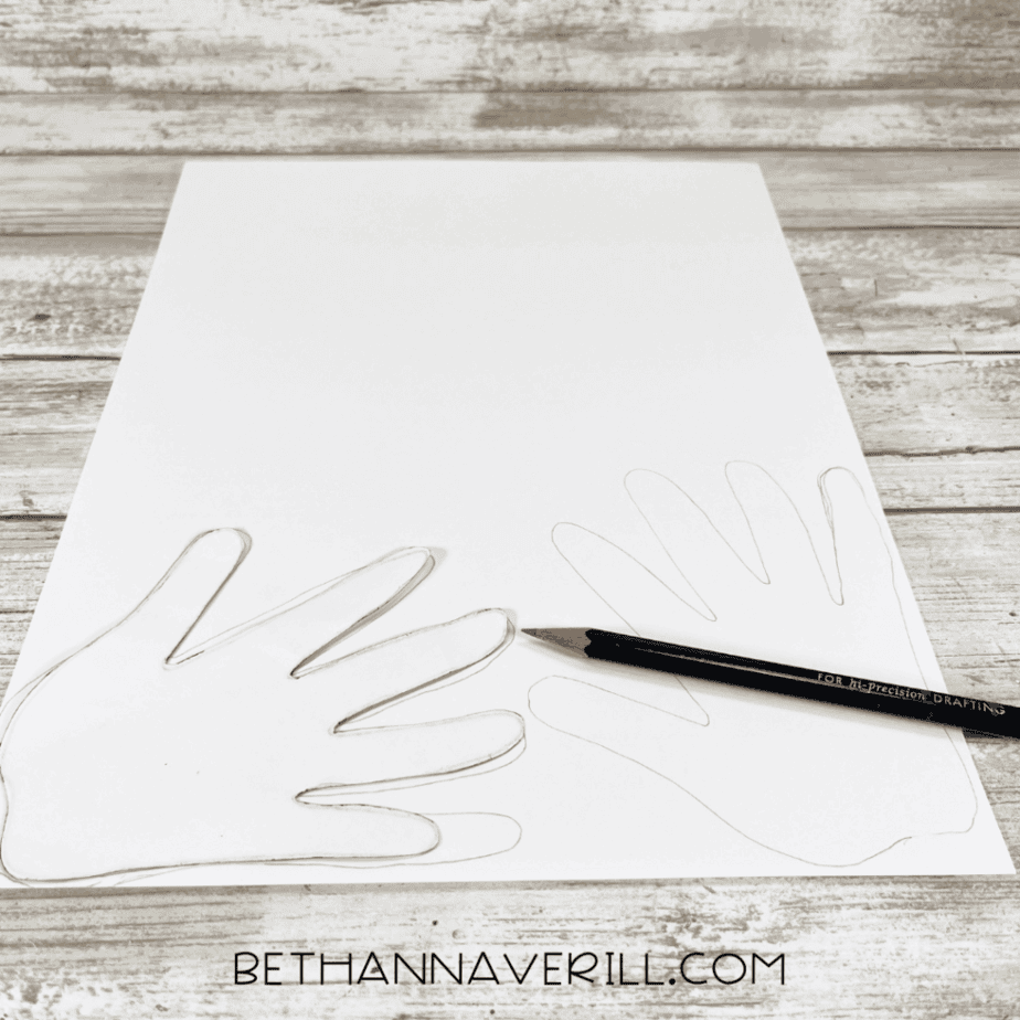 White cardstock with hand outlines traced in pencil next to a black pencil.