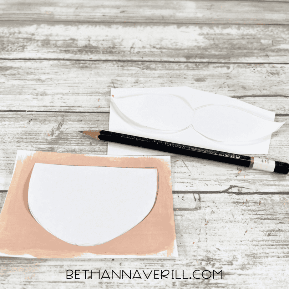 White cardstock shape traced on beige-painted paper with a pencil nearby.