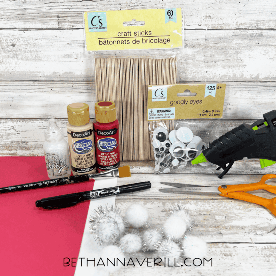 Craft supplies for Santa popsicle stick craft including jumbo craft sticks, acrylic paint, googly eyes, pom poms, glitter glue, scissors, and cardstock.