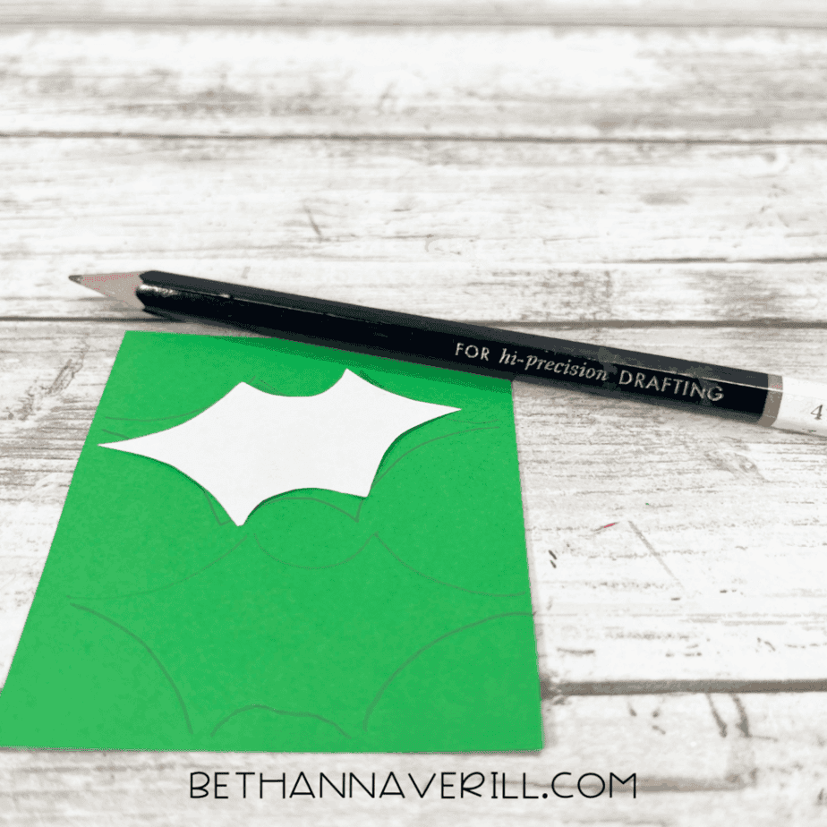 Tracing holly leaf patterns onto green cardstock with a pencil for the Santa craft decoration.
