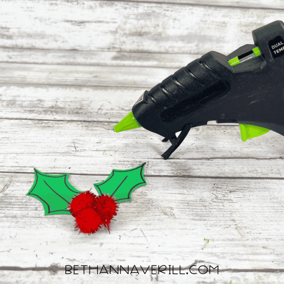 Attaching holly leaves and red pom pom berries with a glue gun for the Santa hat decoration.