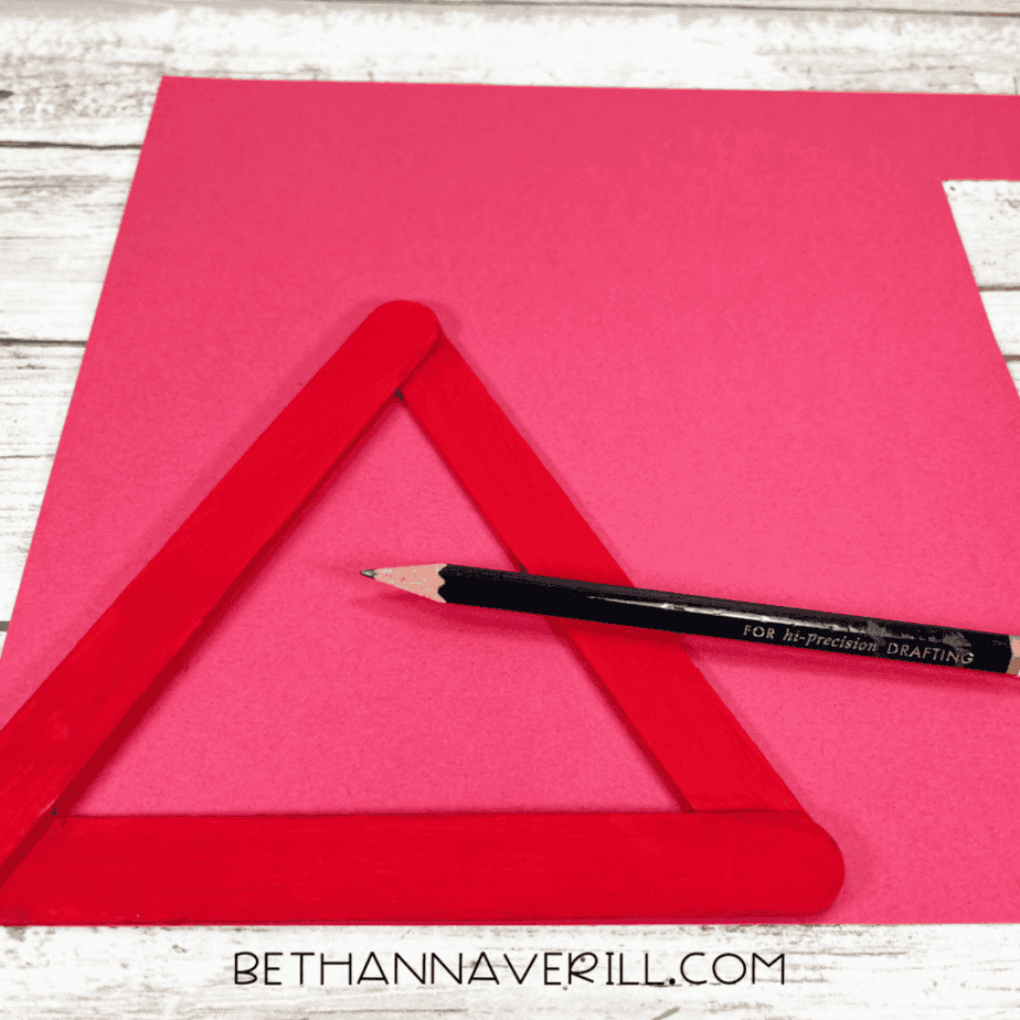 Red cardstock background with painted craft stick Santa hat positioned and ready for assembly.