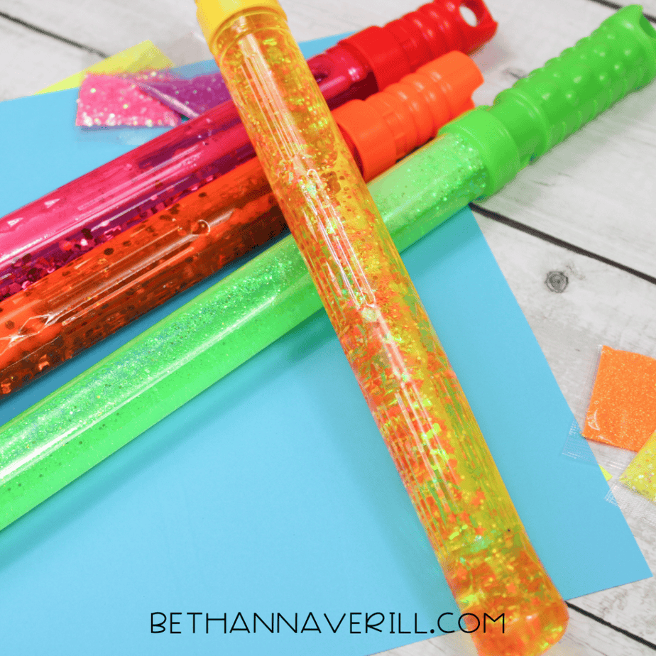 Four finished glitter sensory bubble wands in red, yellow, green, and pink