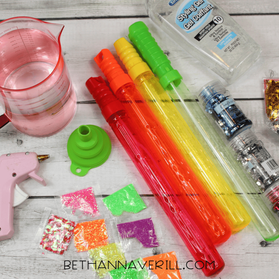 Supplies for bubble wands sensory bottle including clear gel, glitter packets, colorful bubble tubes, measuring cup, funnel, and hot glue gun
