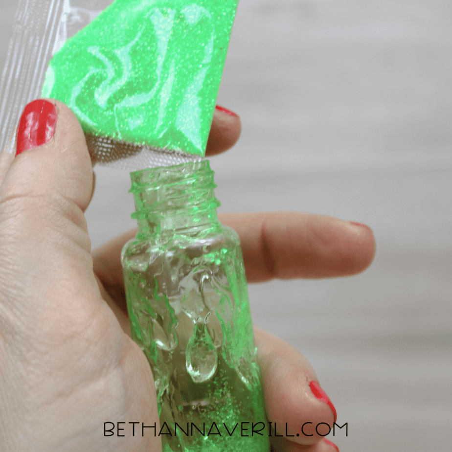 Green glitter being poured into bubble wand tube for sensory bottle