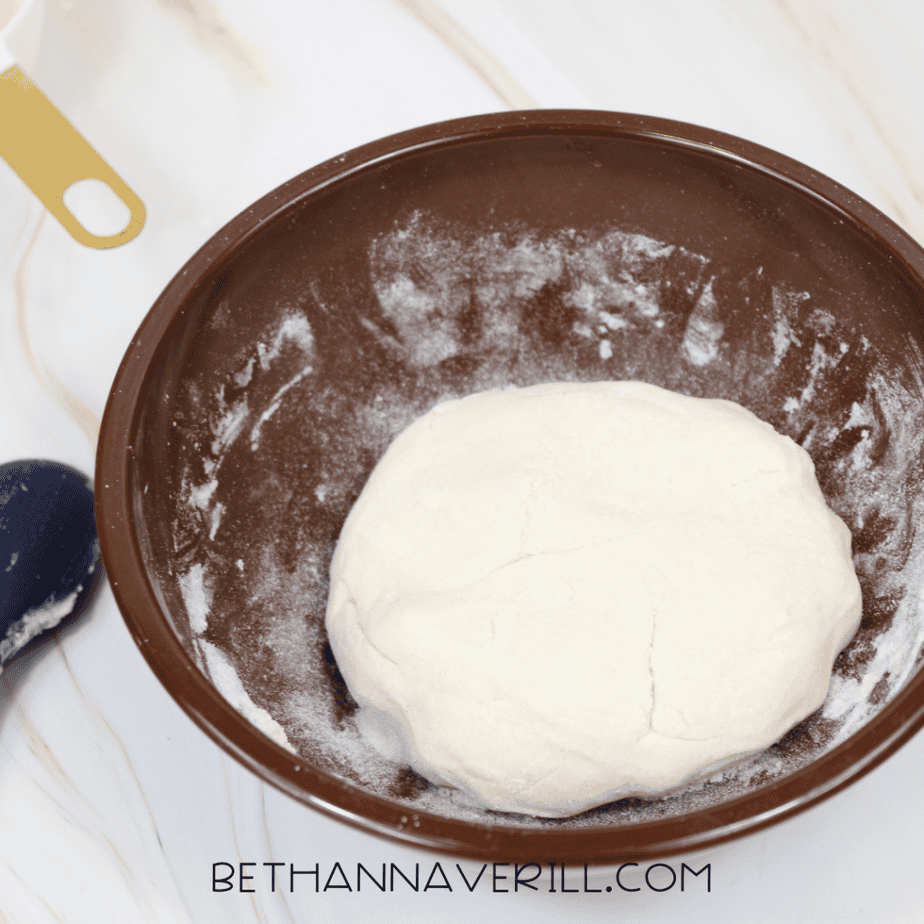 Smooth ball of freshly mixed salt dough resting inside a lightly floured brown bowl.