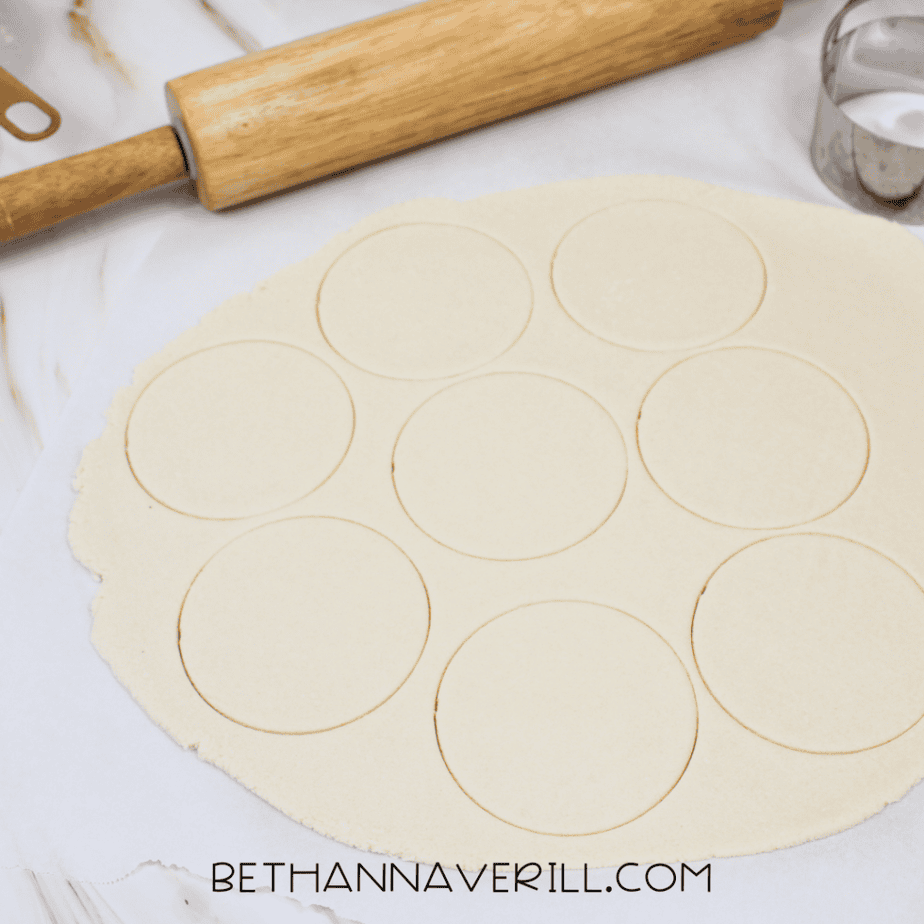 Rolled out sheet of salt dough with circle shapes cut out using a round cookie cutter and a rolling pin nearby.