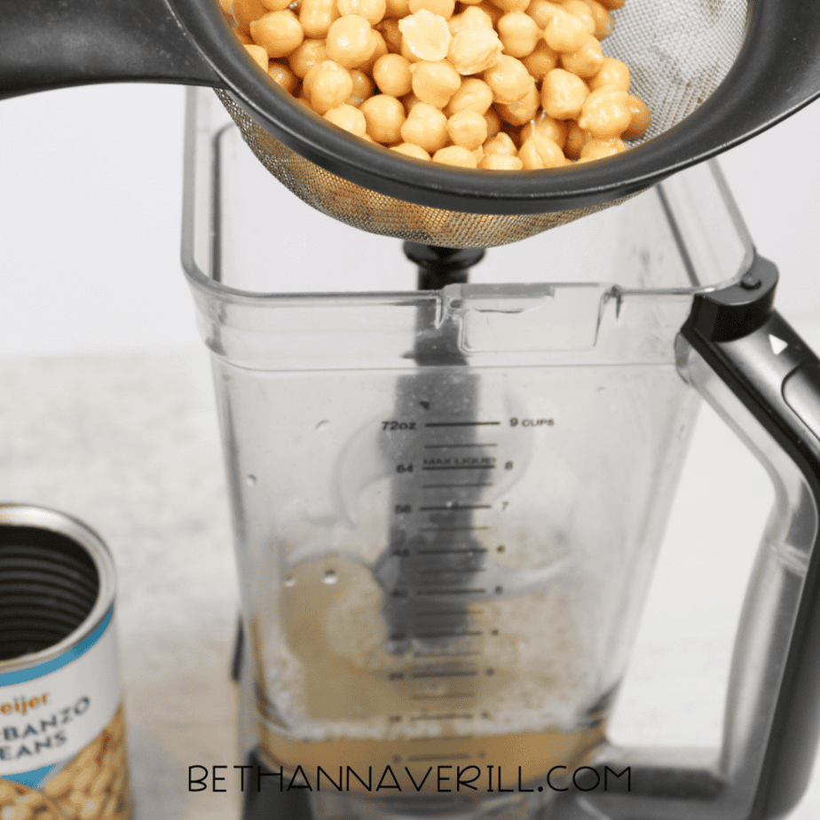 Garbanzo beans being drained through a mesh strainer into a blender container to collect the aquafaba liquid.