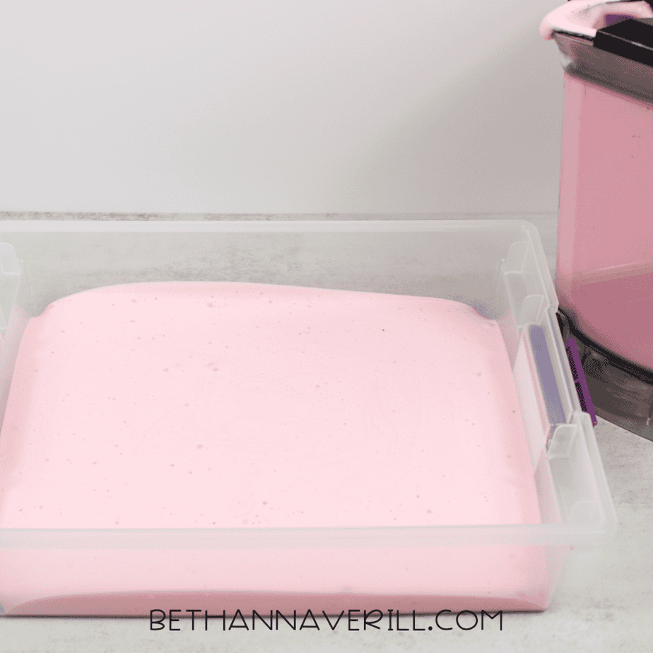 A shallow plastic bin filled with fluffy pink aquafaba foam spread evenly across the bottom.