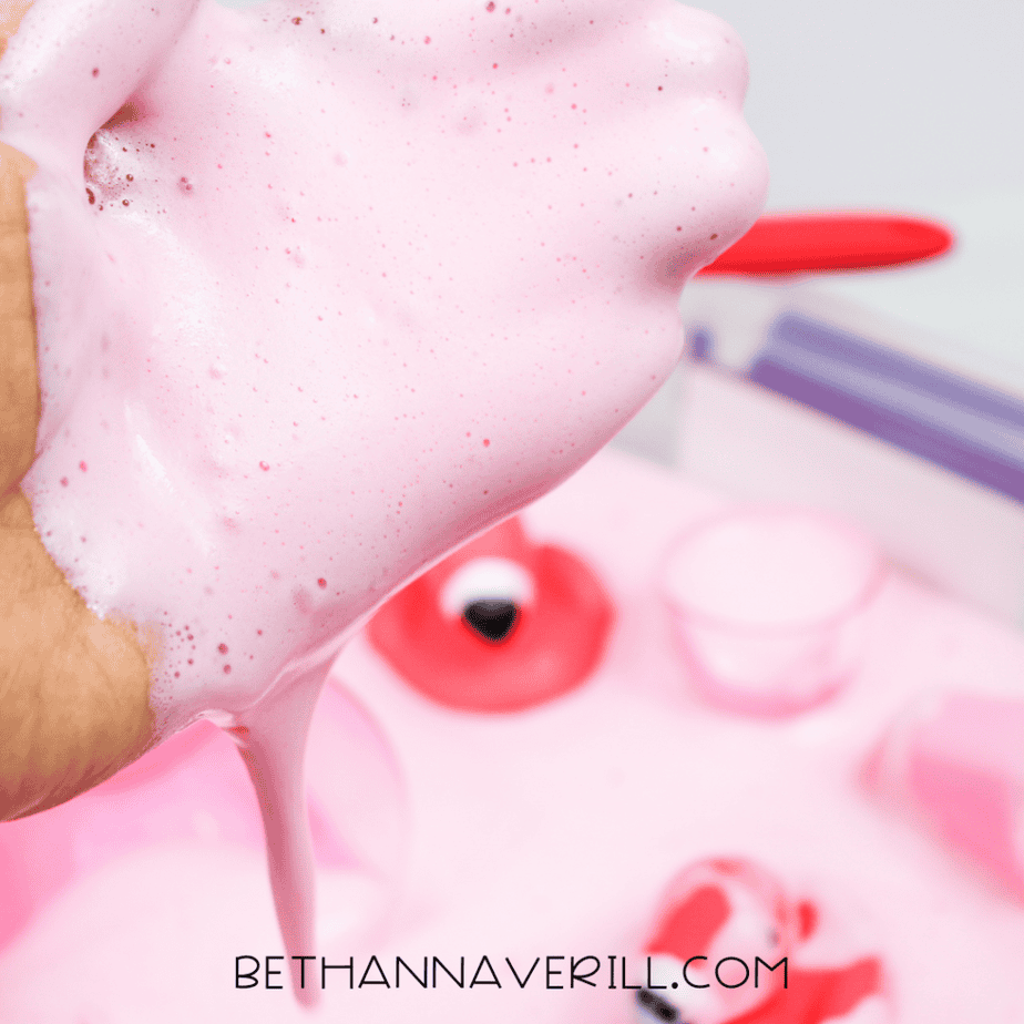 A hand stretching soft, airy pink aquafaba foam, showing its light and bubbly texture.