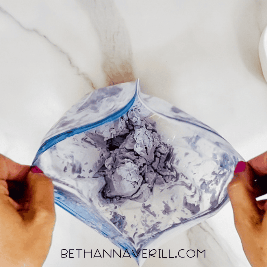 Open plastic bag revealing partially mixed lavender cloud dough forming soft clumps.