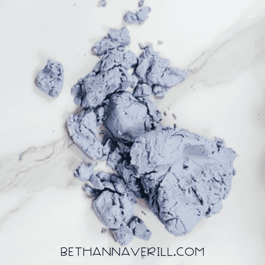 Purple cloud dough mixture poured onto a white marble surface in crumbly pieces before kneading.