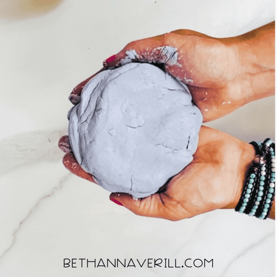 Hands holding a smooth ball of lavender-colored cloud dough.