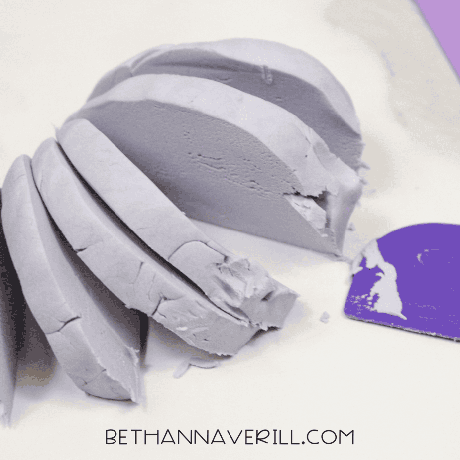 Lavender cloud dough sliced into smooth sections with a plastic scraper, revealing the soft interior.