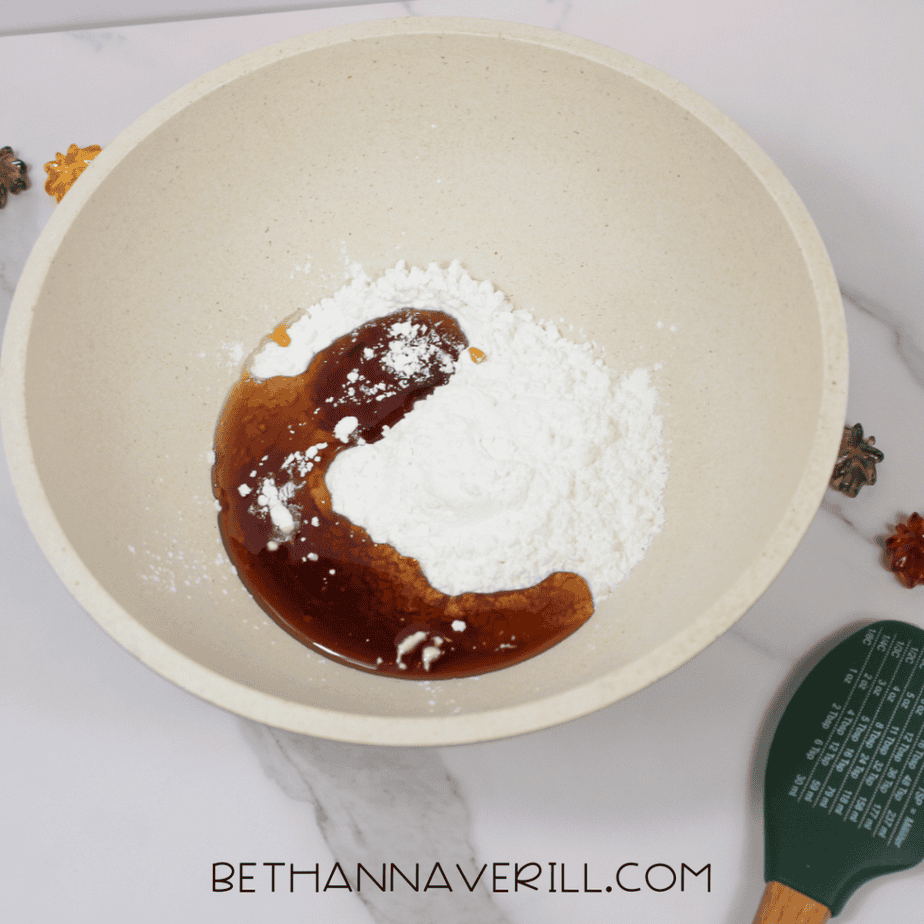 Maple syrup and cornstarch added to a large mixing bowl, shown before mixing, with a green spatula resting nearby.