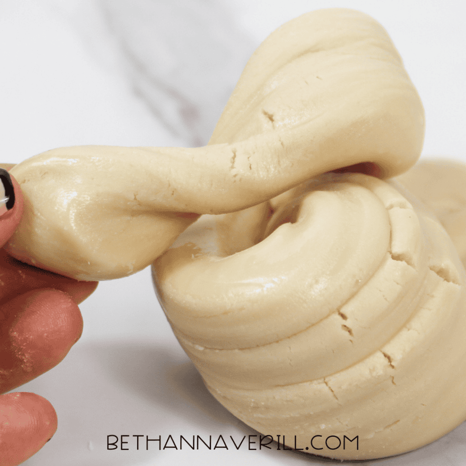 Close-up of maple syrup slime being stretched by hand, showing a smooth, soft dough texture.