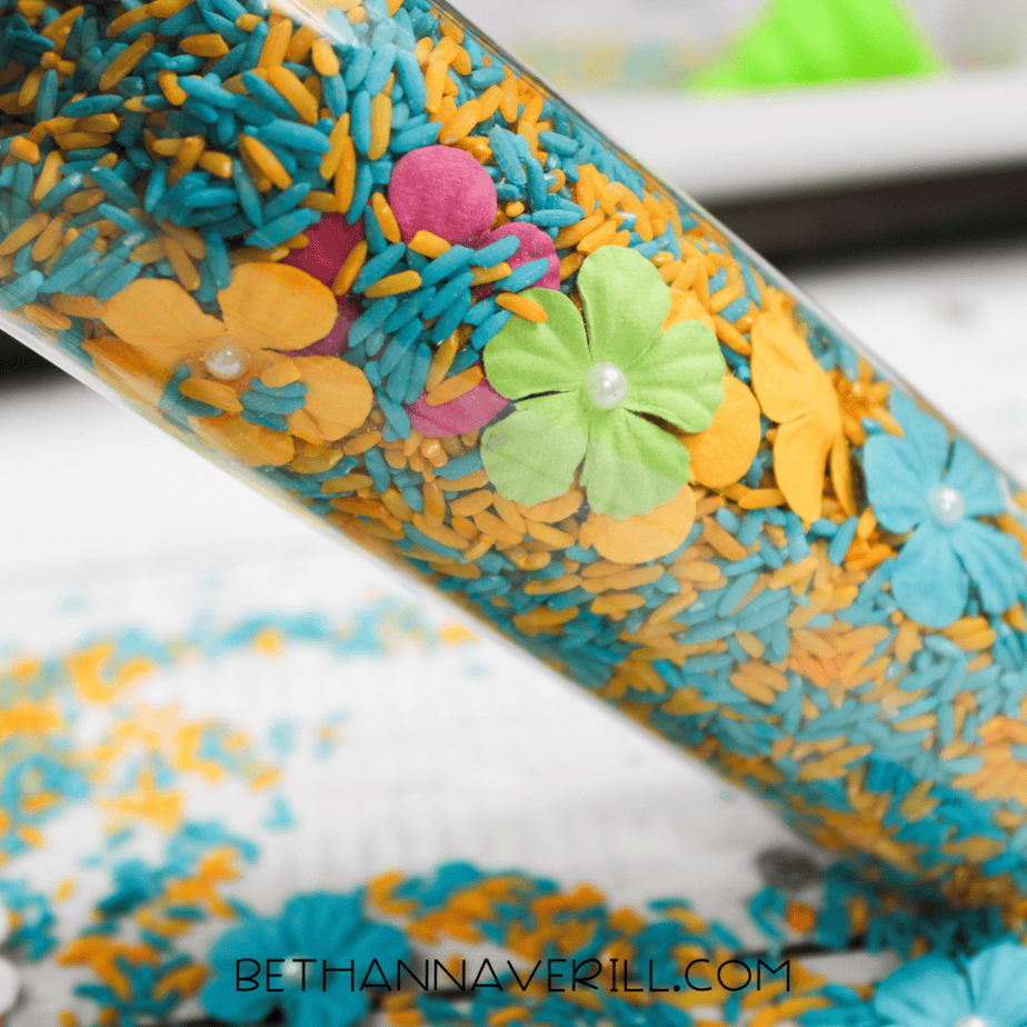 Close-up of clear sensory bottle showing dyed rice and pastel flower embellishments.