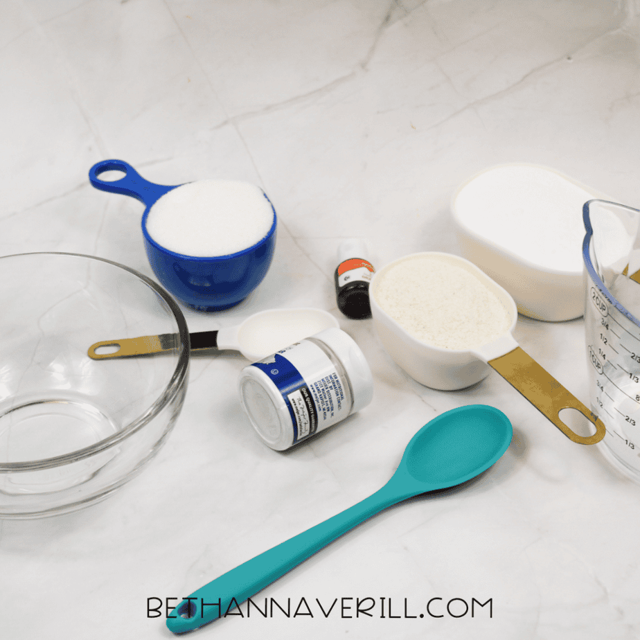 Measuring cups, bowls, a spoon, food coloring, and a liquid measuring cup arranged on a countertop for a sensory play recipe.
