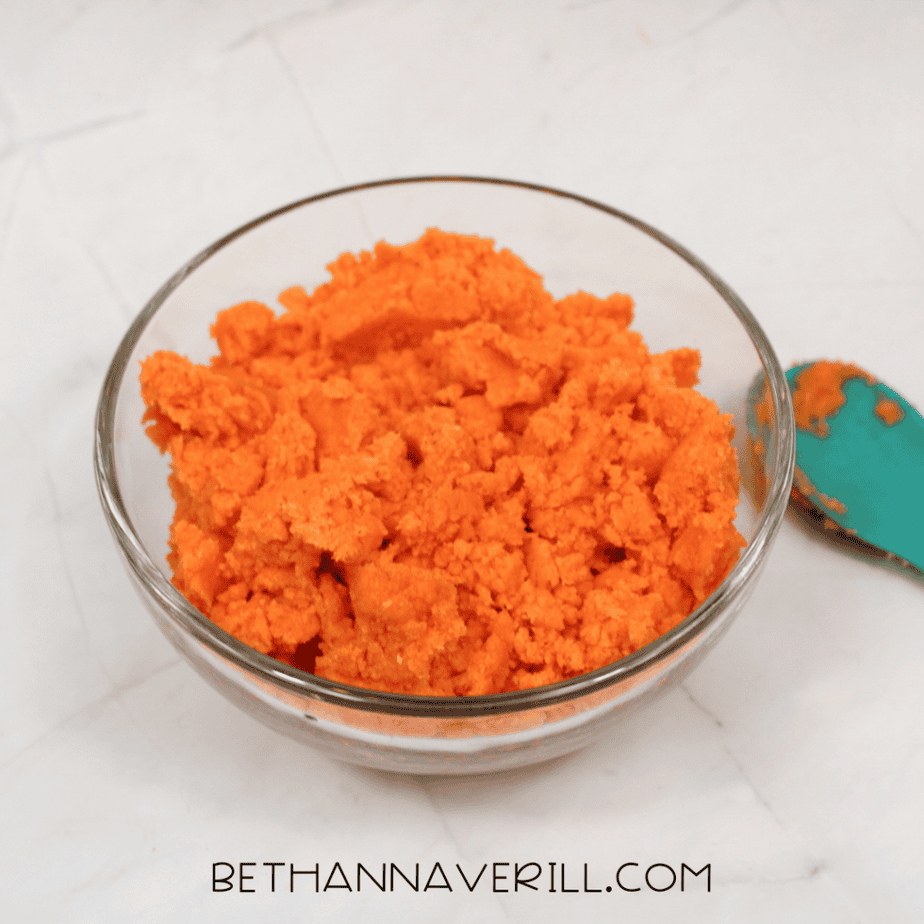 Glass bowl filled with bright orange crumbly mixture after being stirred together.