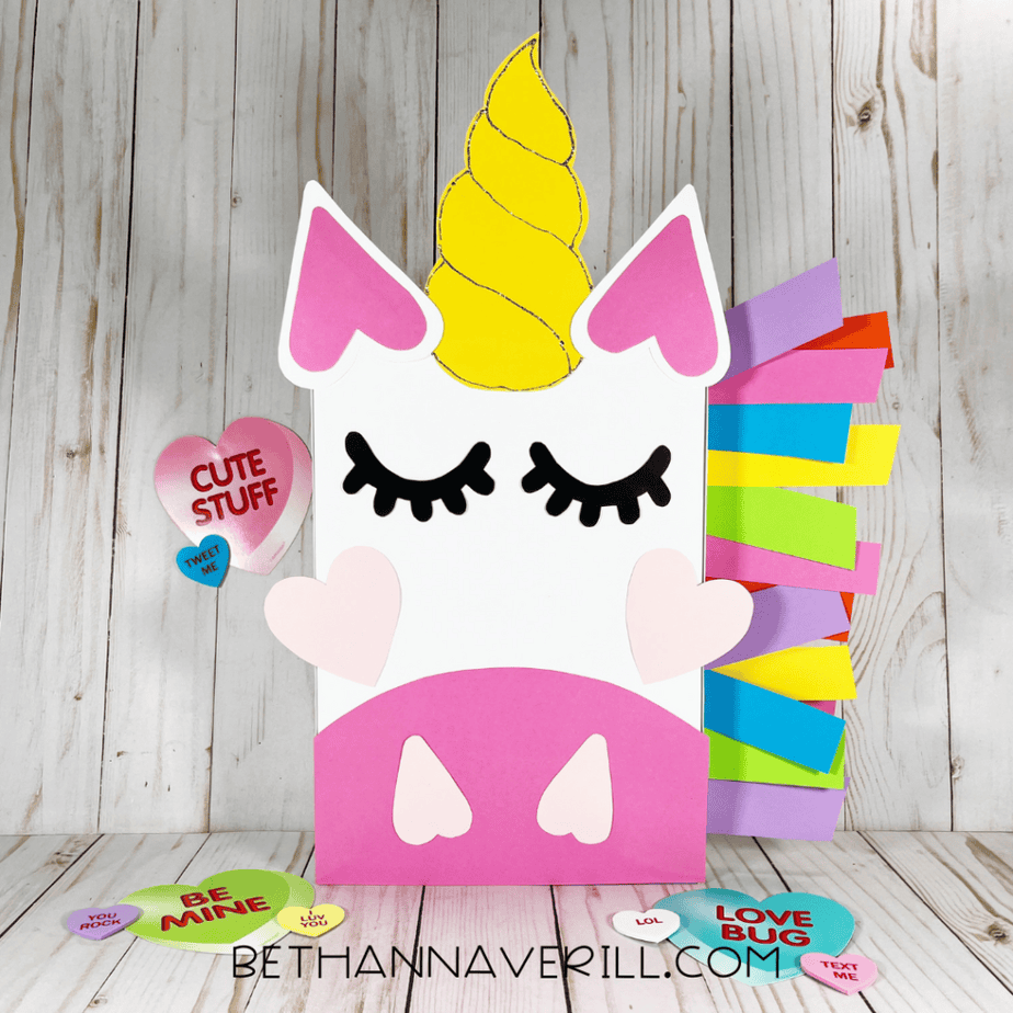 Completed unicorn Valentine’s Day box decorated with a yellow horn, closed eyes with lashes, pink cheeks, heart details, and colorful mane, surrounded by conversation heart candies.