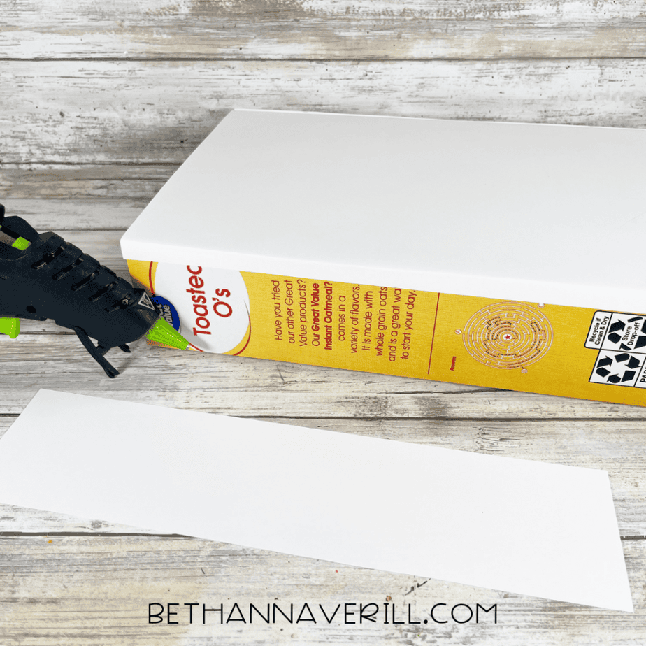 Hot glue gun securing white paper around the side of the cereal box.