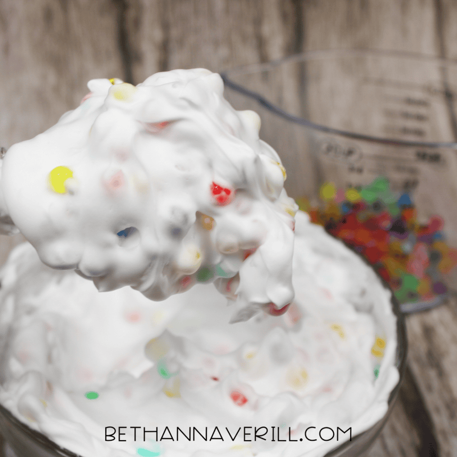 A spoon lifting a scoop of white foam mixed with colorful water beads, showing the texture up close.