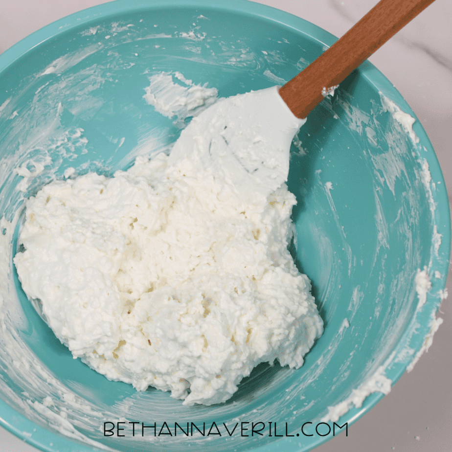 White mixture being stirred inside a teal bowl with a white spatula.