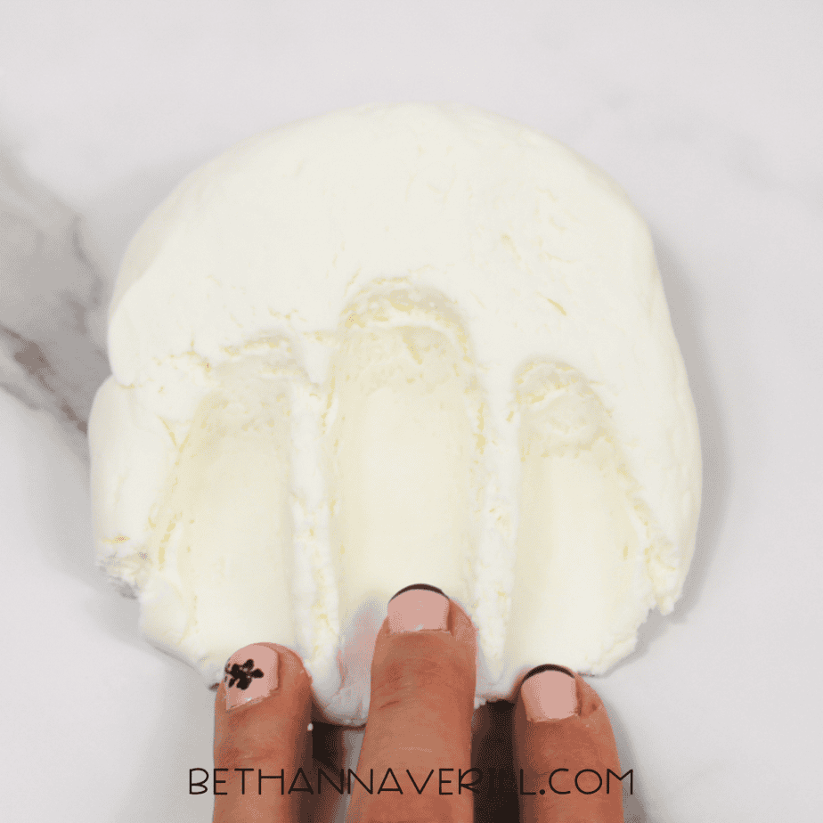 Hand pressing three fingers into a smooth white slime, leaving indentations.